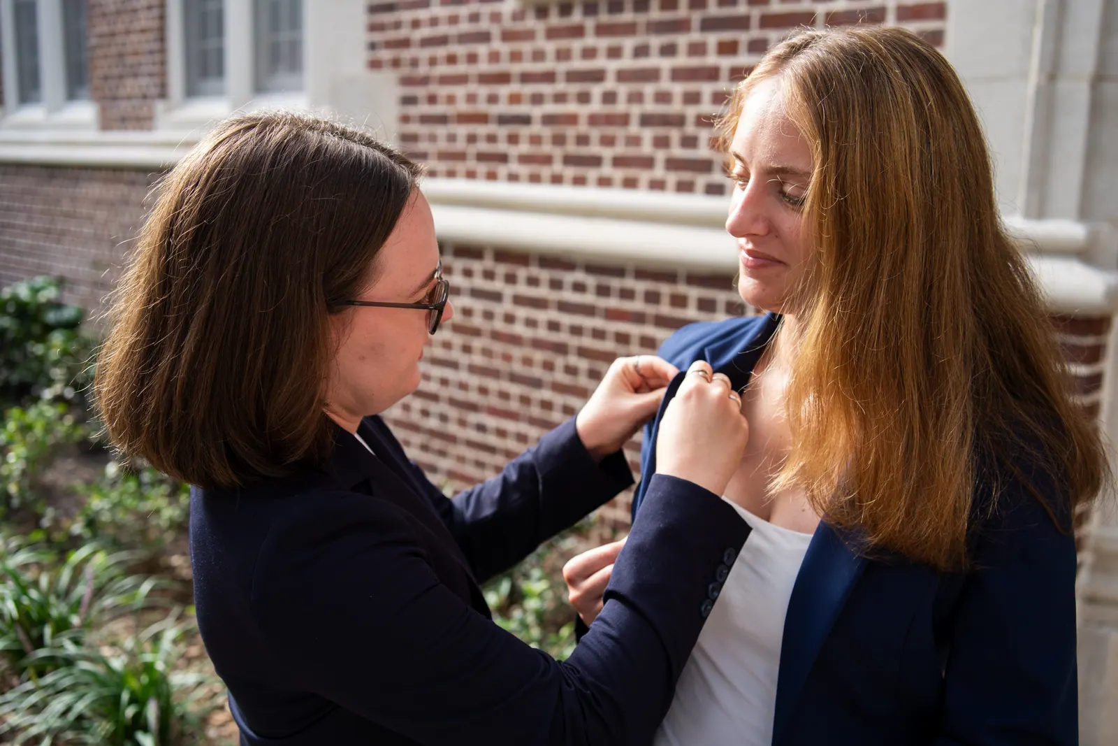 Candid moment: one member pins a badge to another's blazer before a headshot.