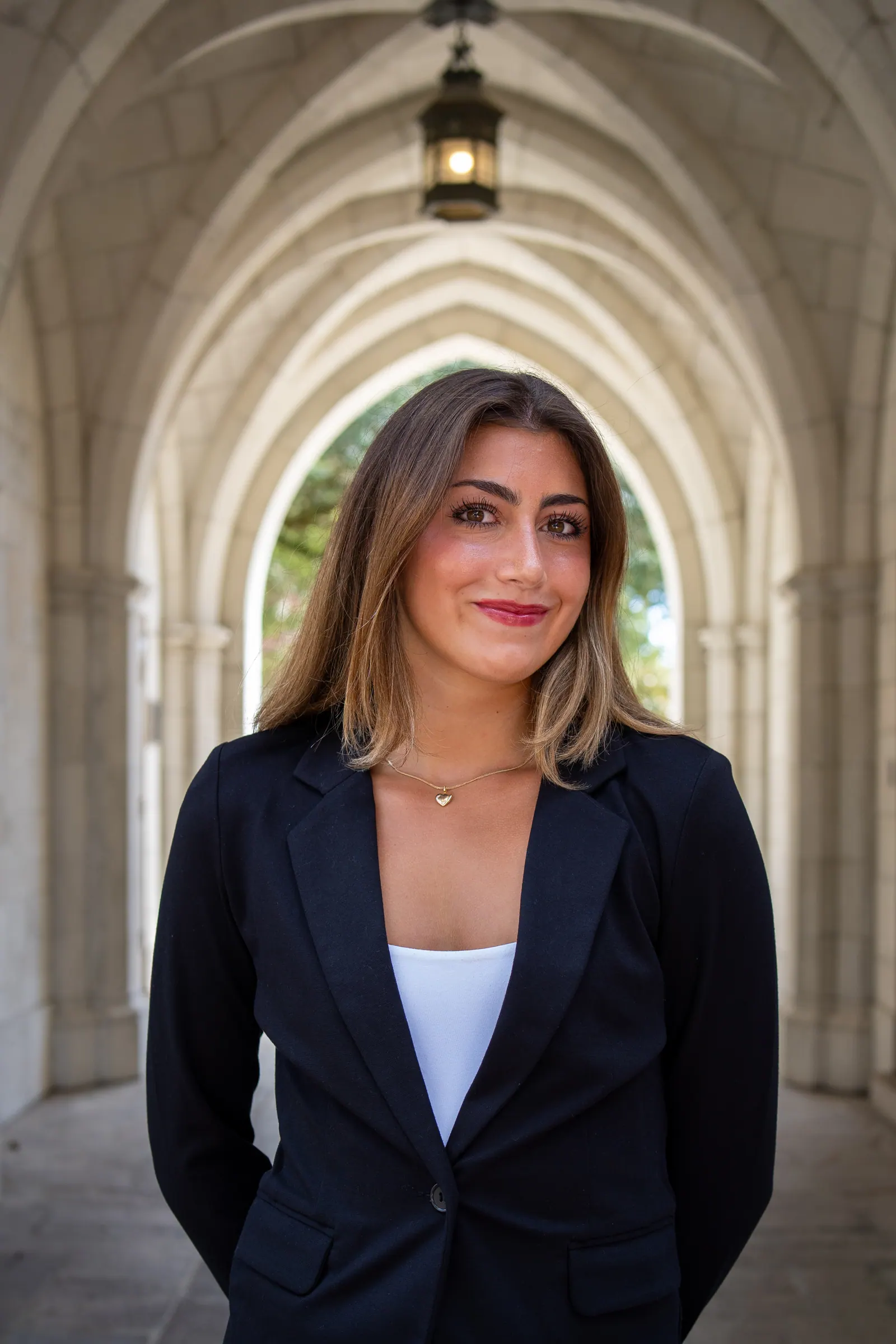 Headshot of a young woman in a black blazer under a vaulted stone archway.