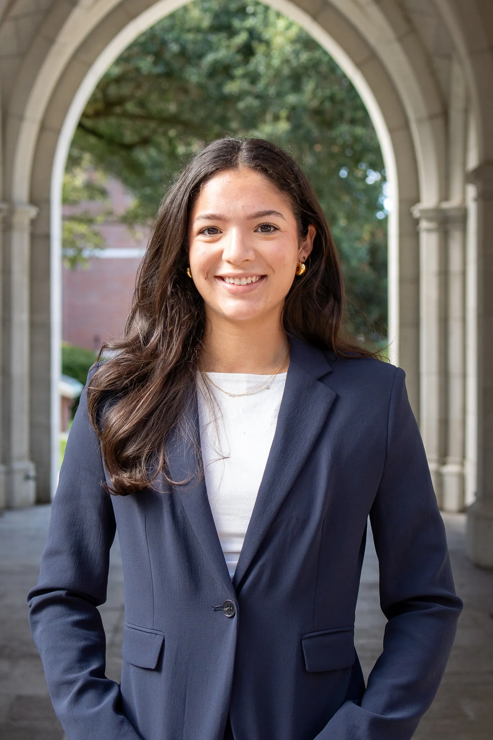 Headshot of a young woman in a navy blazer smiling under a stone archway.