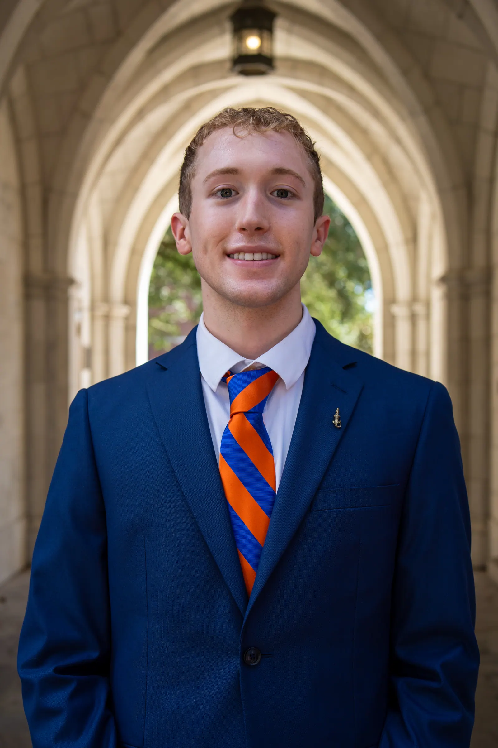 Headshot of a young man in a navy suit and orange-and-blue striped tie.