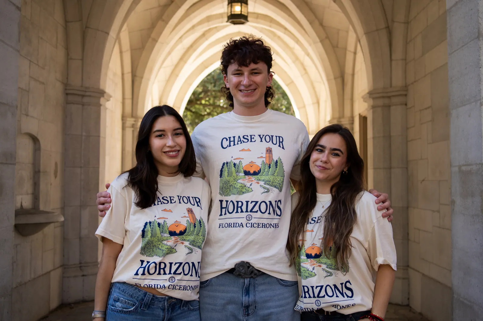 Three Florida Cicerones members in matching 'Chase Your Horizons' shirts under a stone archway.