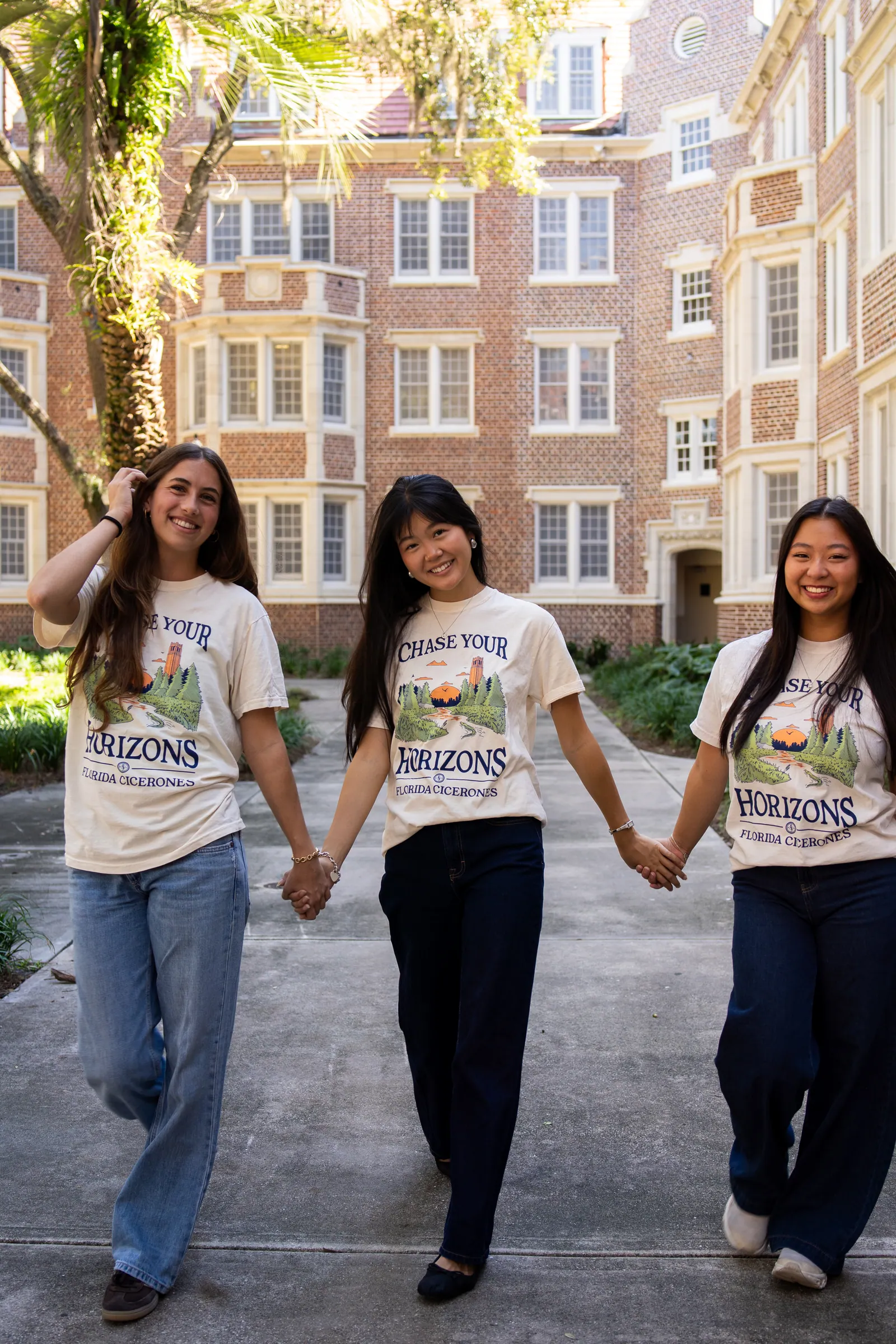 Three Cicerones members hold hands and walk toward the camera in a brick courtyard.