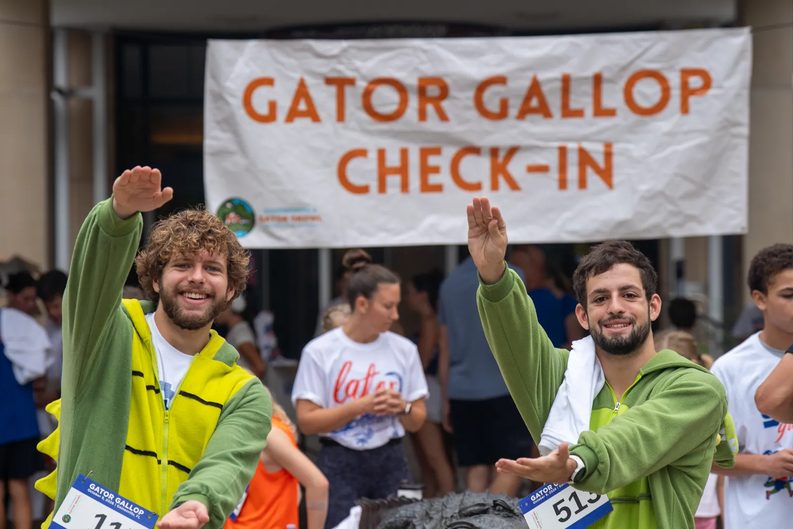 Two runners in green gator costumes do the Gator Chomp under the Gator Gallop check-in banner.