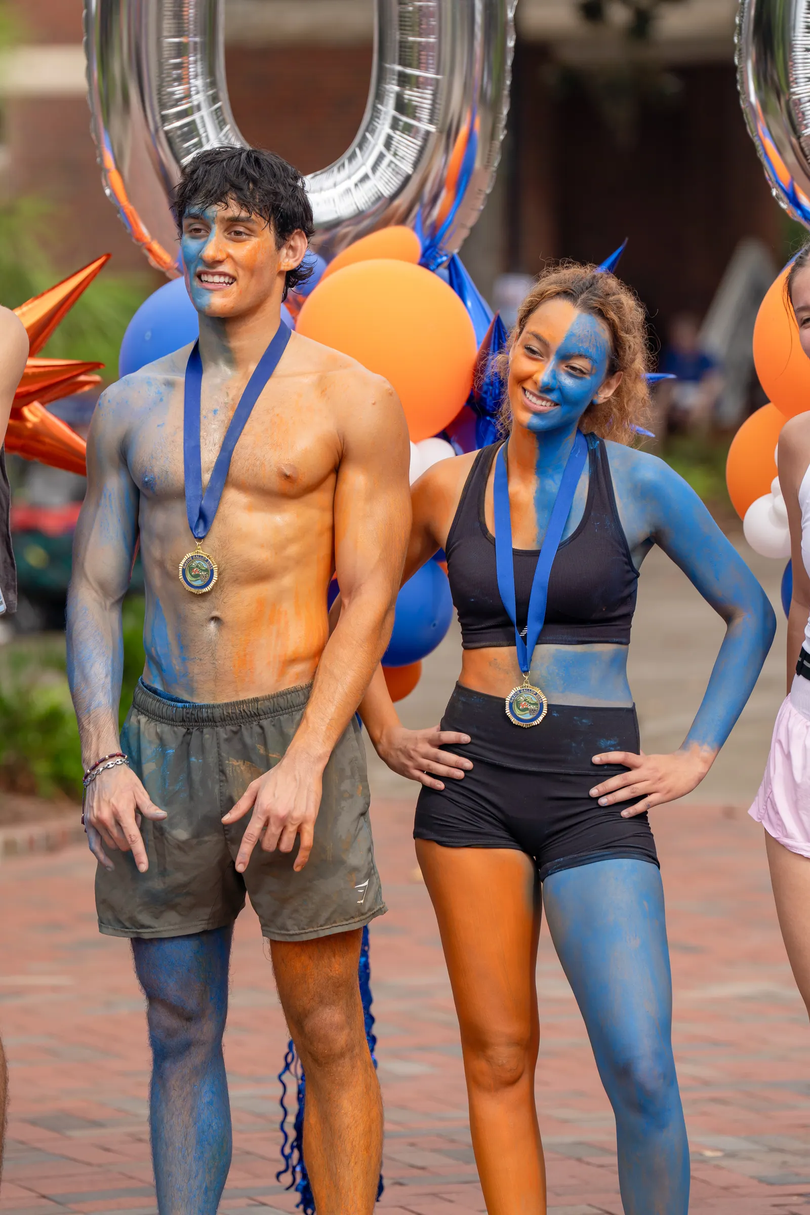 Two finishers in blue and orange body paint pose with their medals in front of balloons.