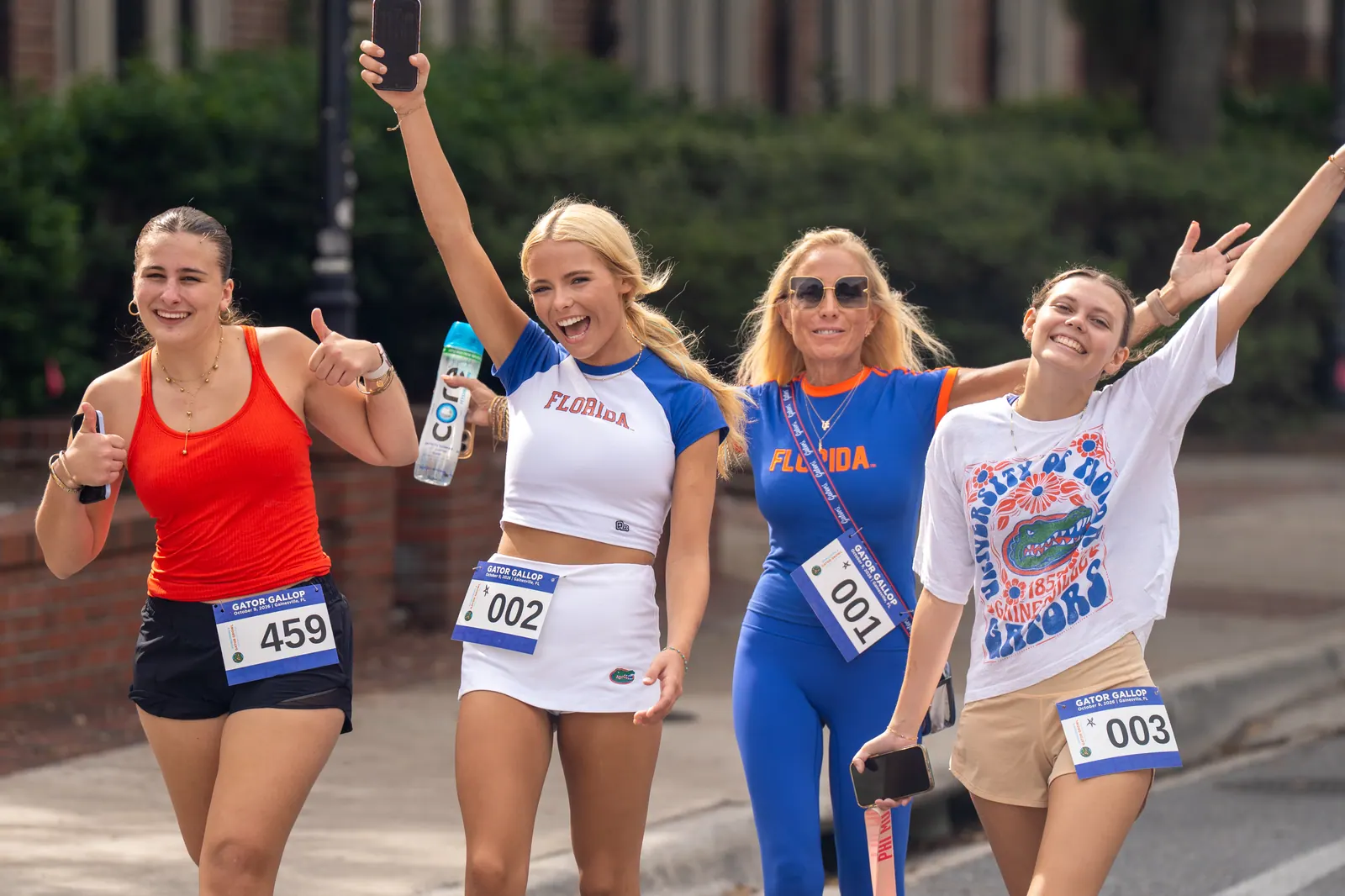 Four friends in orange and blue cheer with arms raised as they run together.