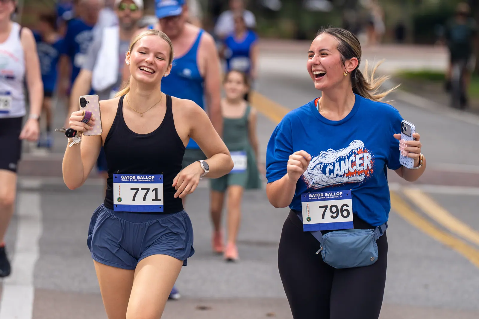 Two runners laugh together mid-race, one holding a phone.
