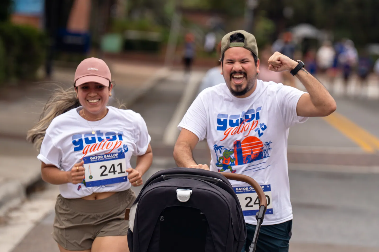 Two runners cheer toward the camera, one pushing a stroller.