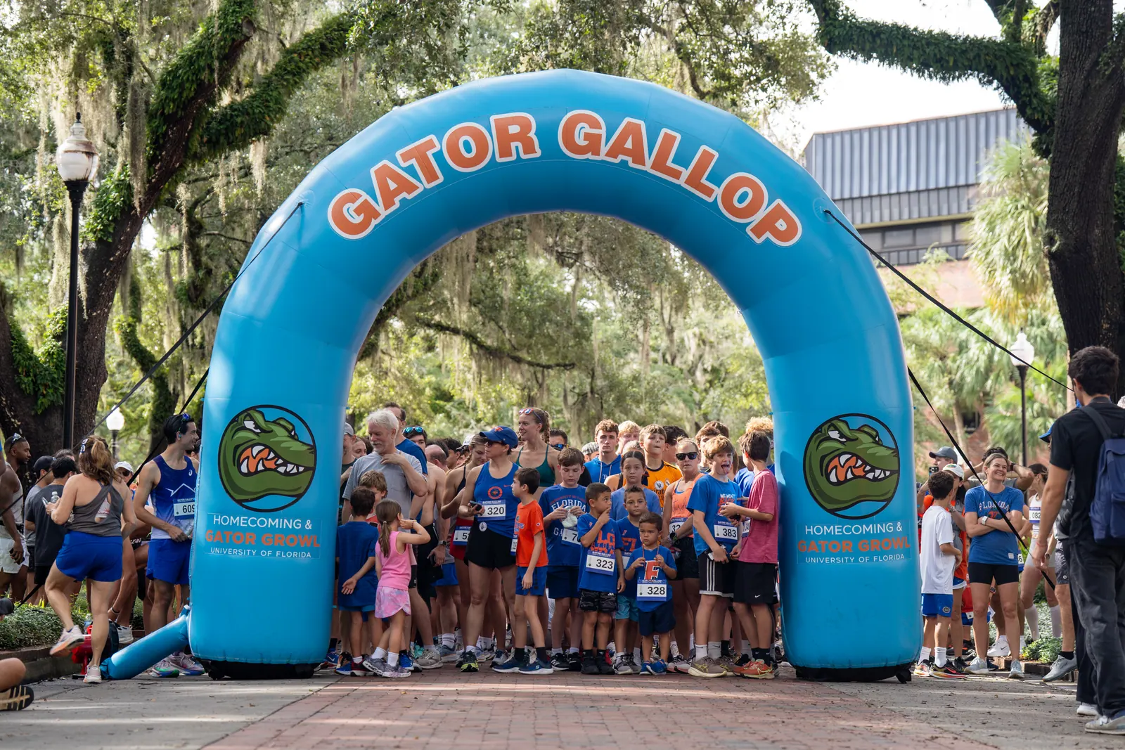 Runners pack the start line beneath the inflatable Gator Gallop arch under oak trees.