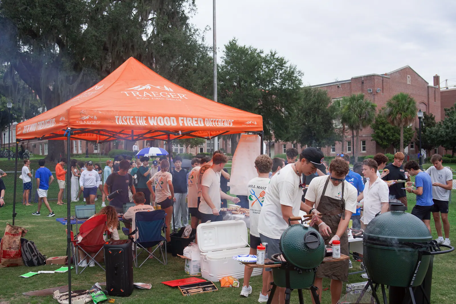 Wide view of the cookout: an orange tent, smokers, and a crowd of students on the grass.