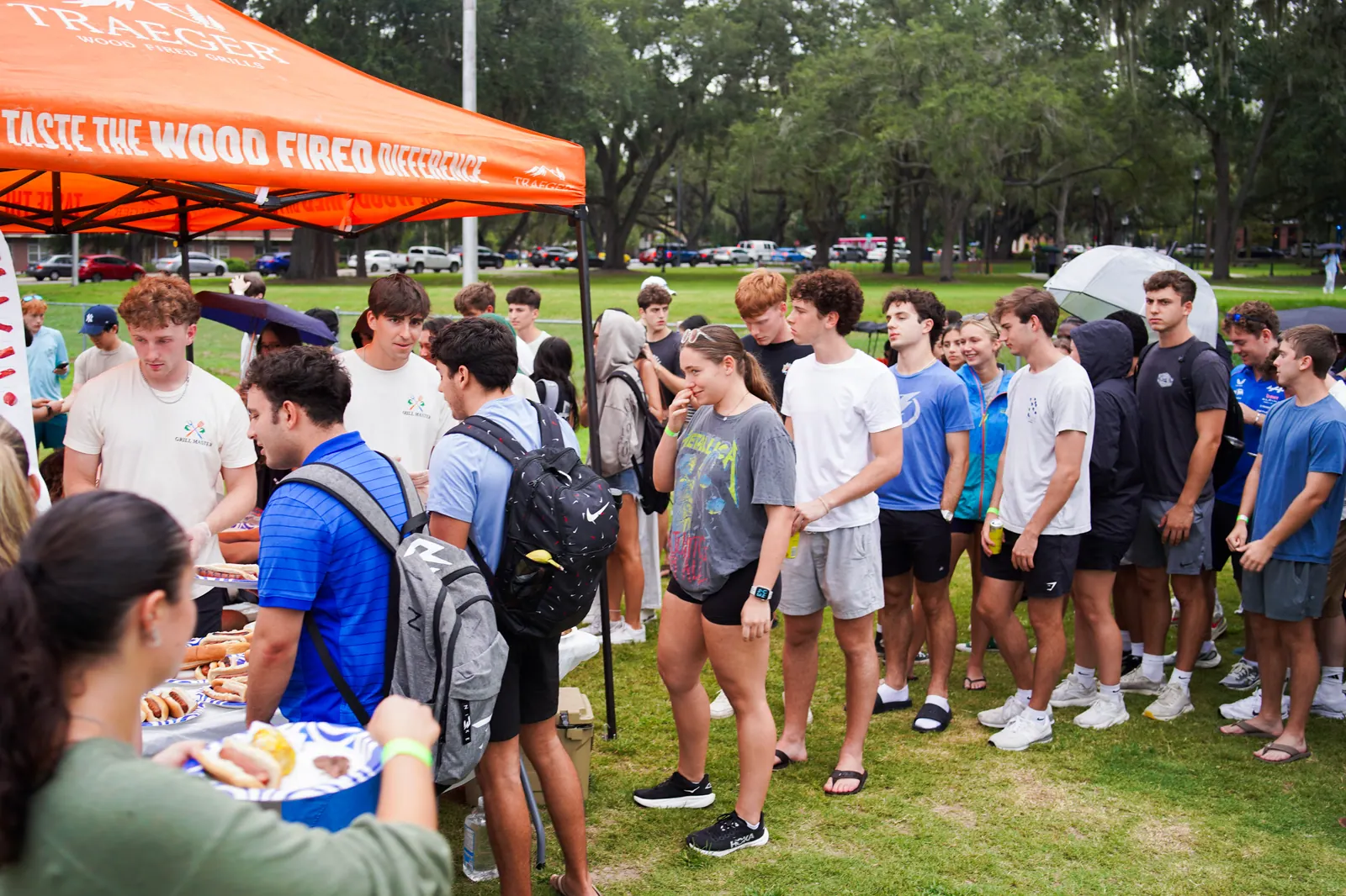 A long line of students waits on the lawn for food.