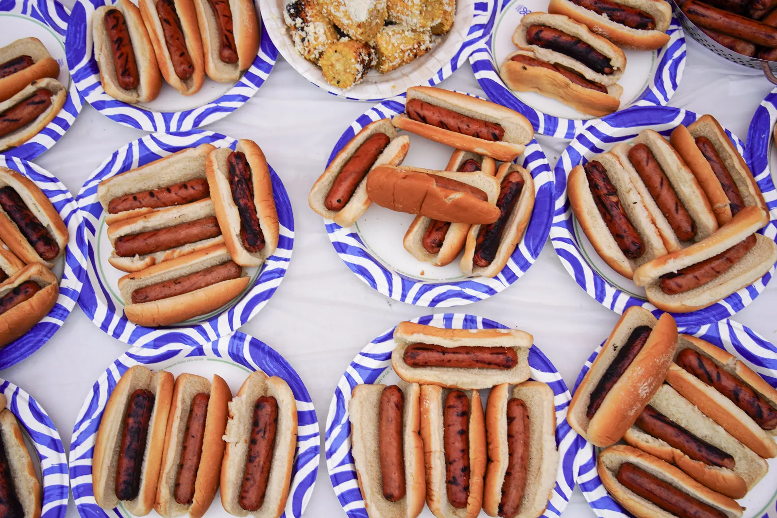Overhead view of rows of hot dogs on blue-and-white paper plates.