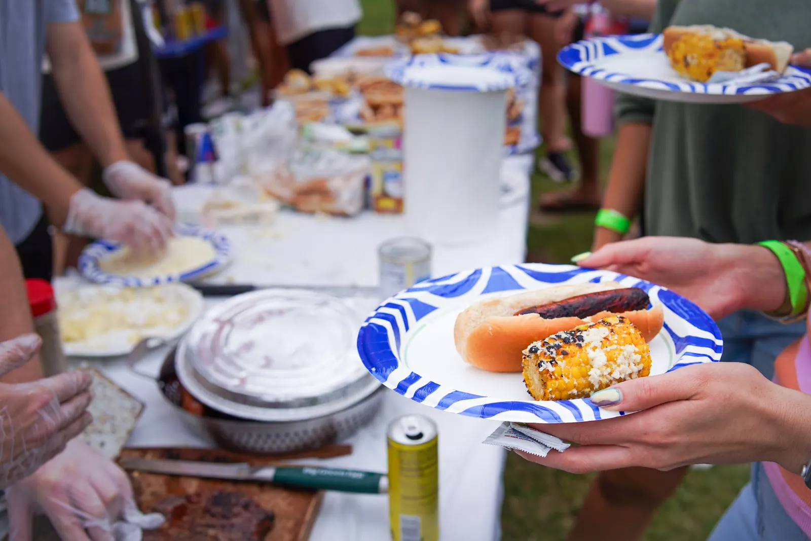 A plate with a hot dog and grilled corn is handed across the serving table.