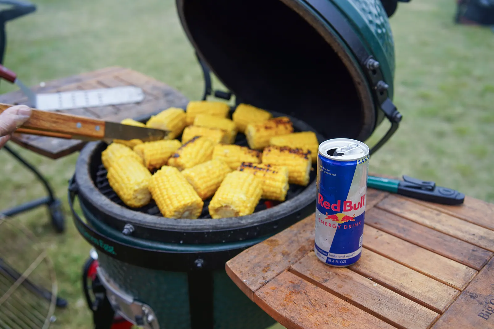 Ears of corn charring on a ceramic grill next to an energy drink on the side shelf.
