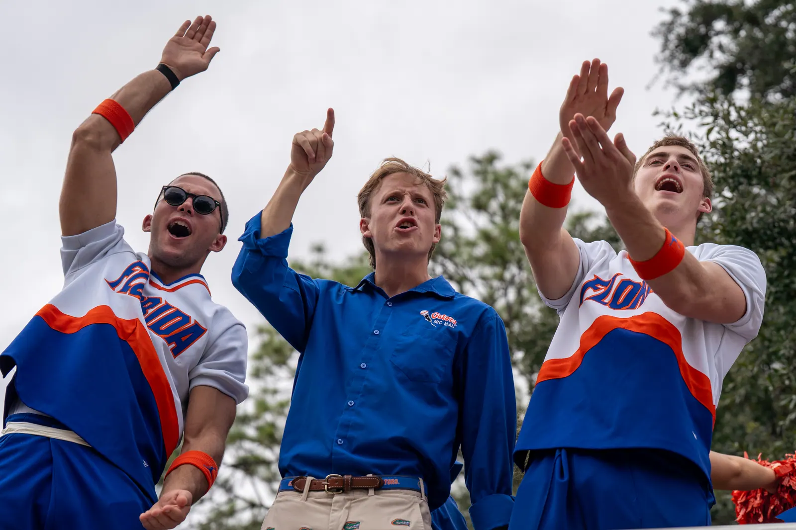 Three Florida cheerleaders shout and wave from atop a parade float.