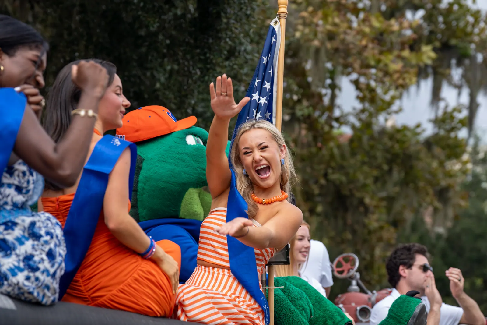 A woman with a sash laughs and waves from a float beside an American flag.