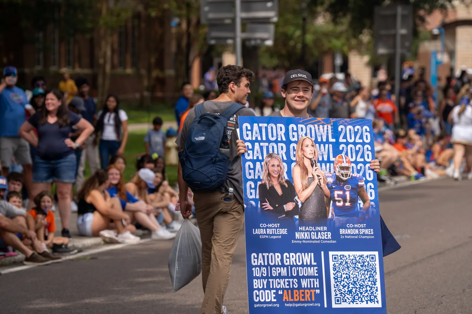 Two students carry a Gator Growl 2026 poster past spectators on the curb.