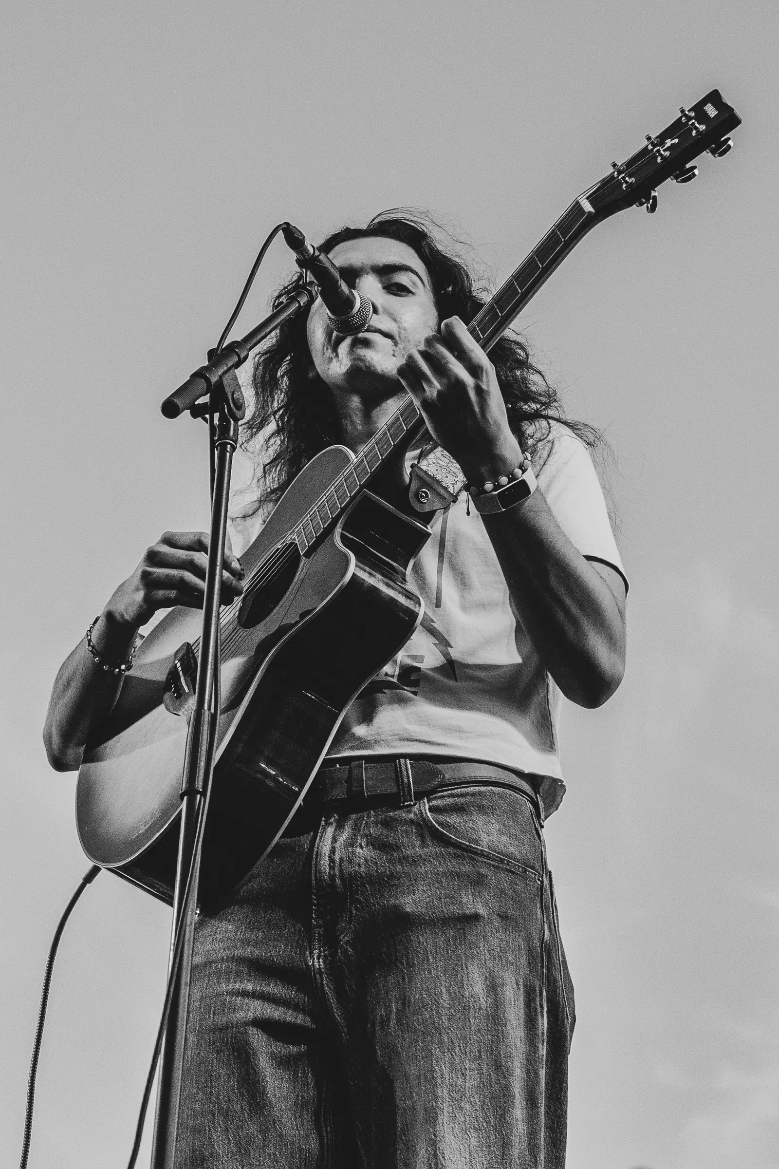 Black and white, low-angle shot of a guitarist singing at the microphone with an acoustic guitar.