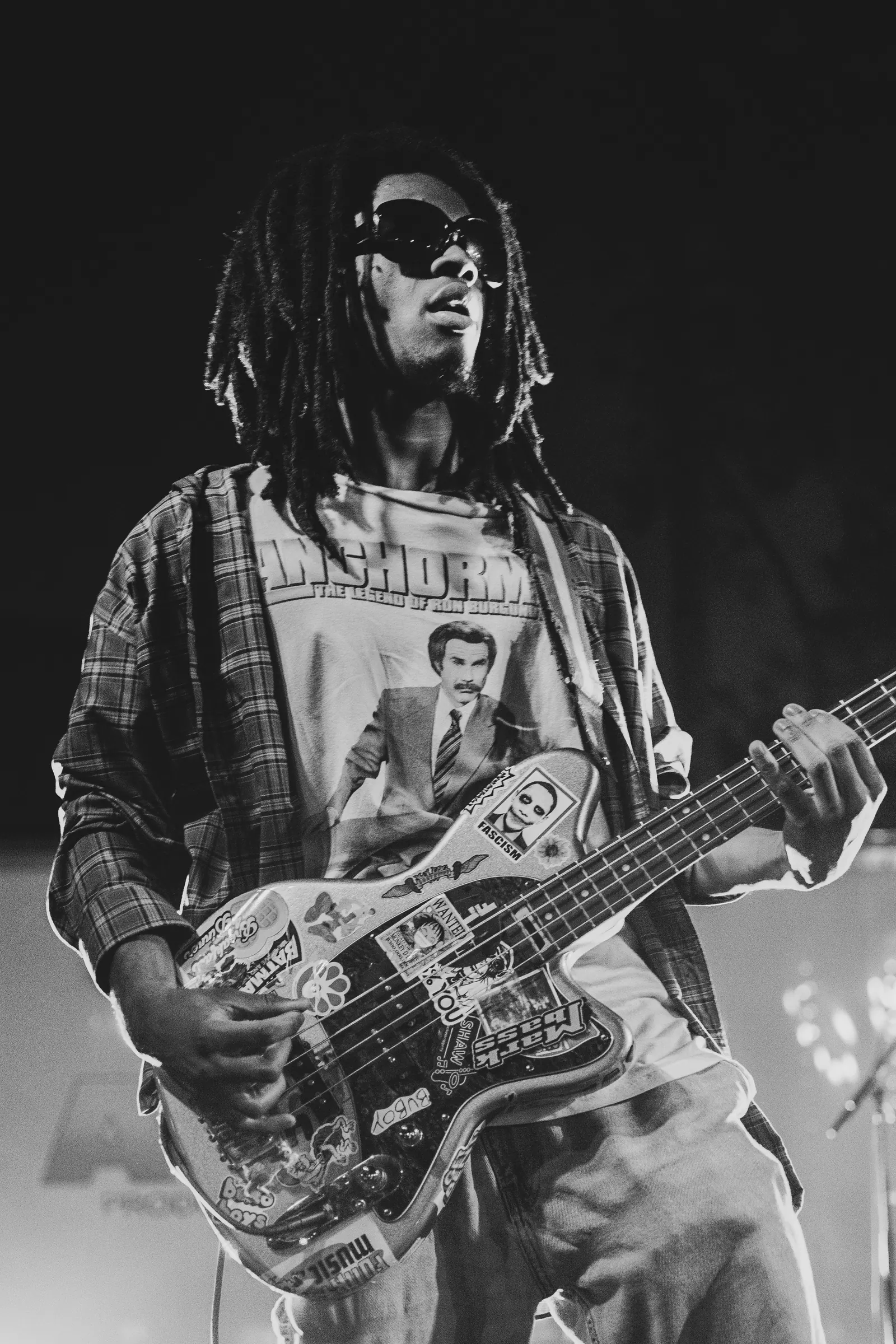Black and white portrait of a bassist in sunglasses with a sticker-covered bass.