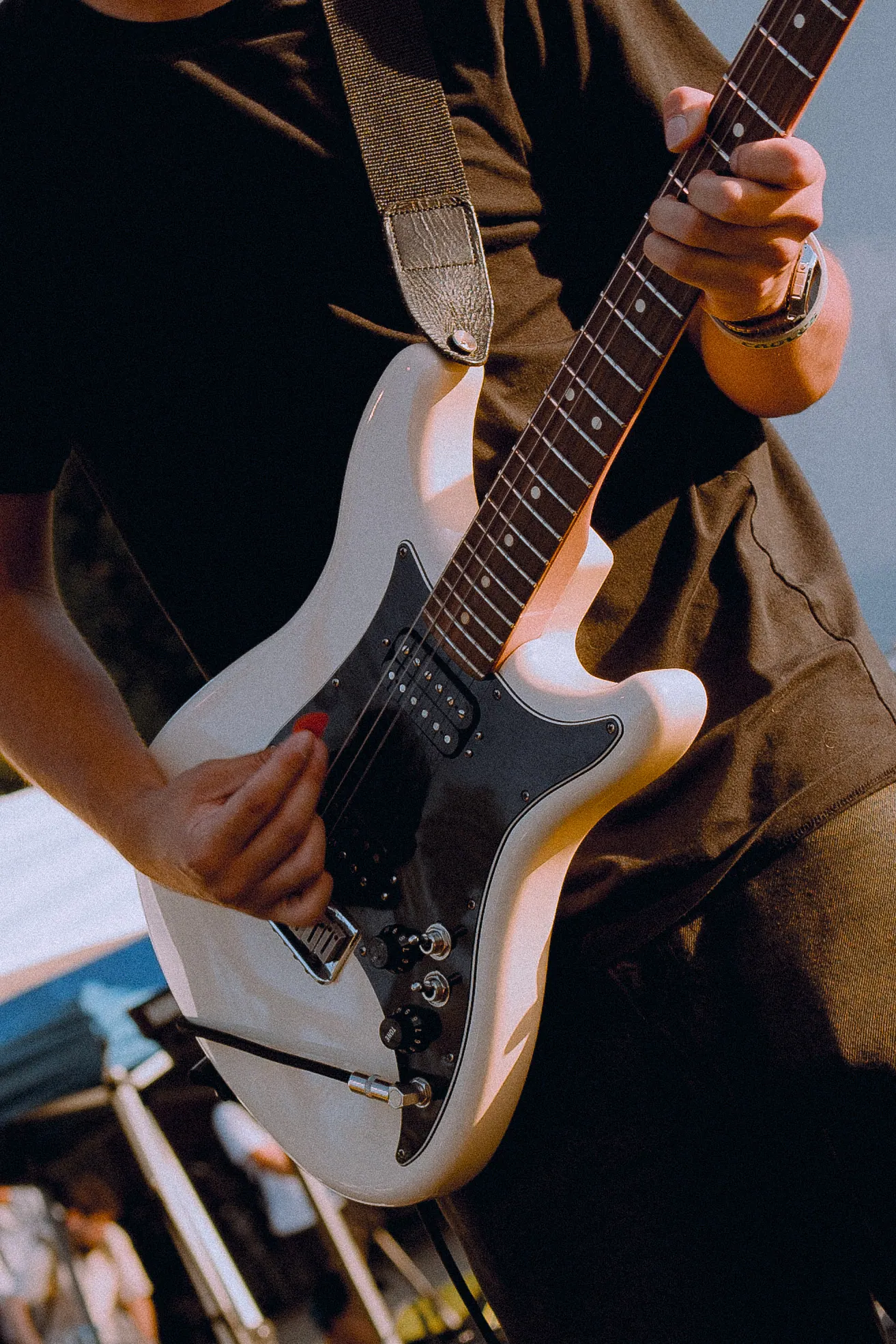 Close crop of hands on a cream electric guitar in warm late-afternoon light.