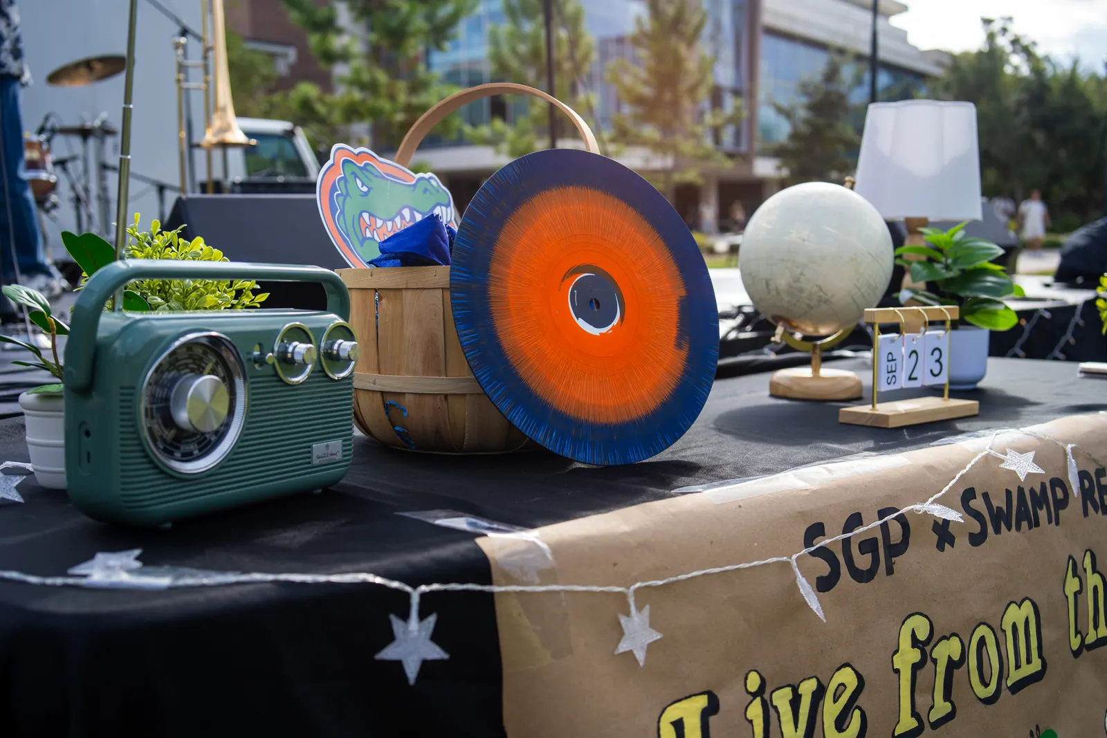 A table set for Live From the Lawn: a green retro radio, a blue and orange vinyl record, a globe, and a flip calendar showing September 23.
