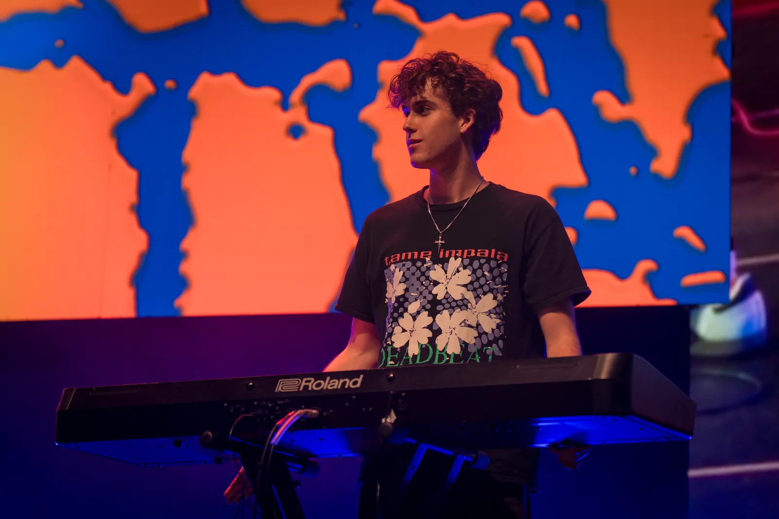 The keyboardist at a Roland keyboard, looking off stage, with the orange and blue screen behind.