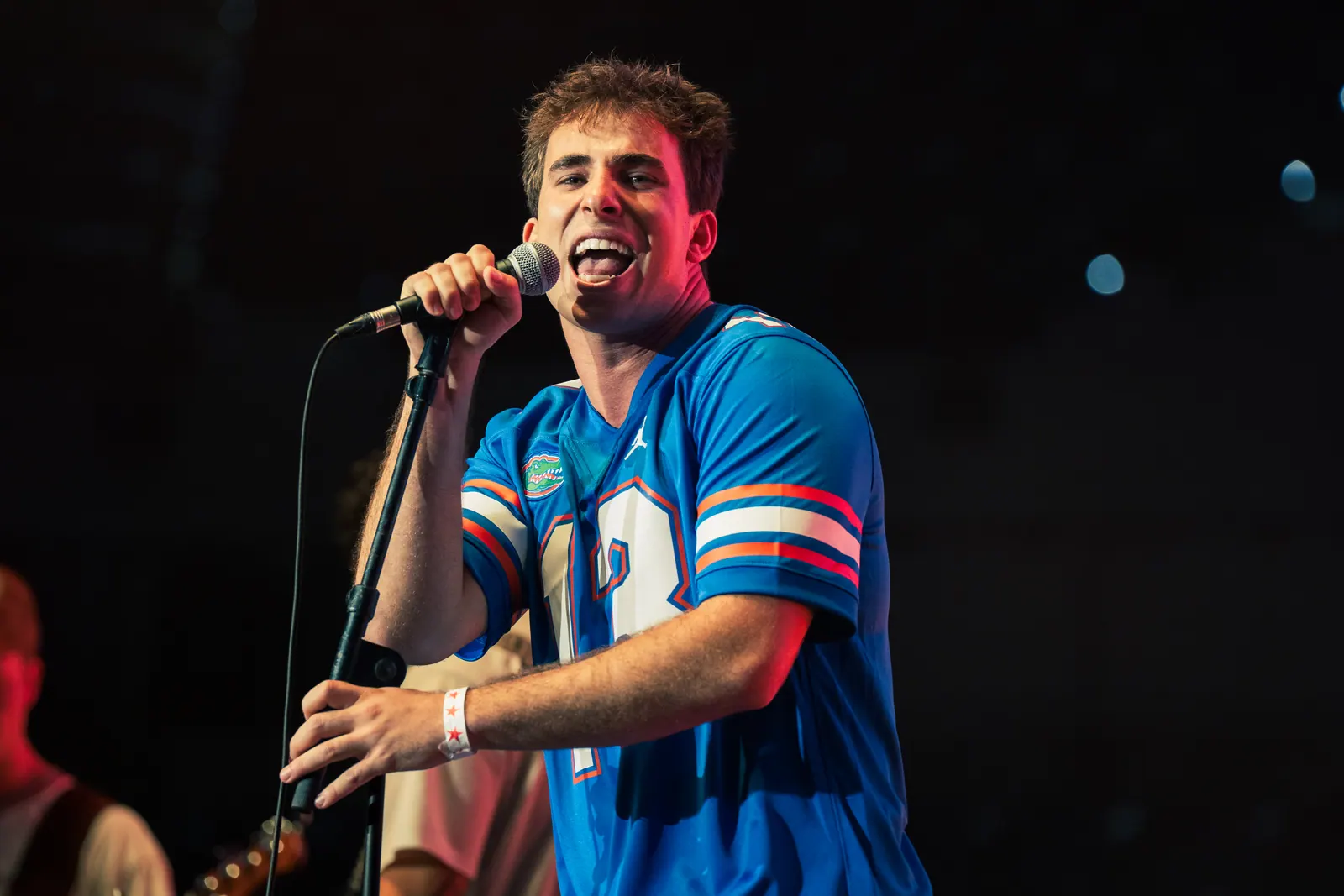 The vocalist grinning mid-song under dark stage light, gripping the microphone stand.