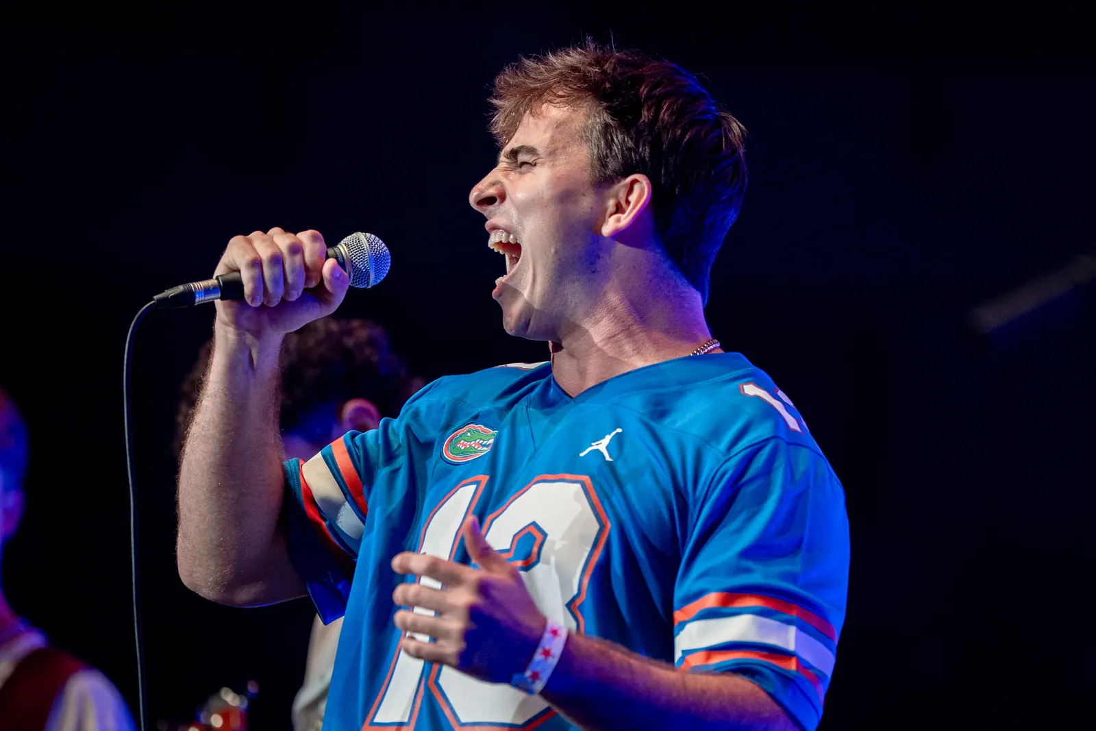 Profile of the vocalist singing with eyes shut, lit in blue against a black background.
