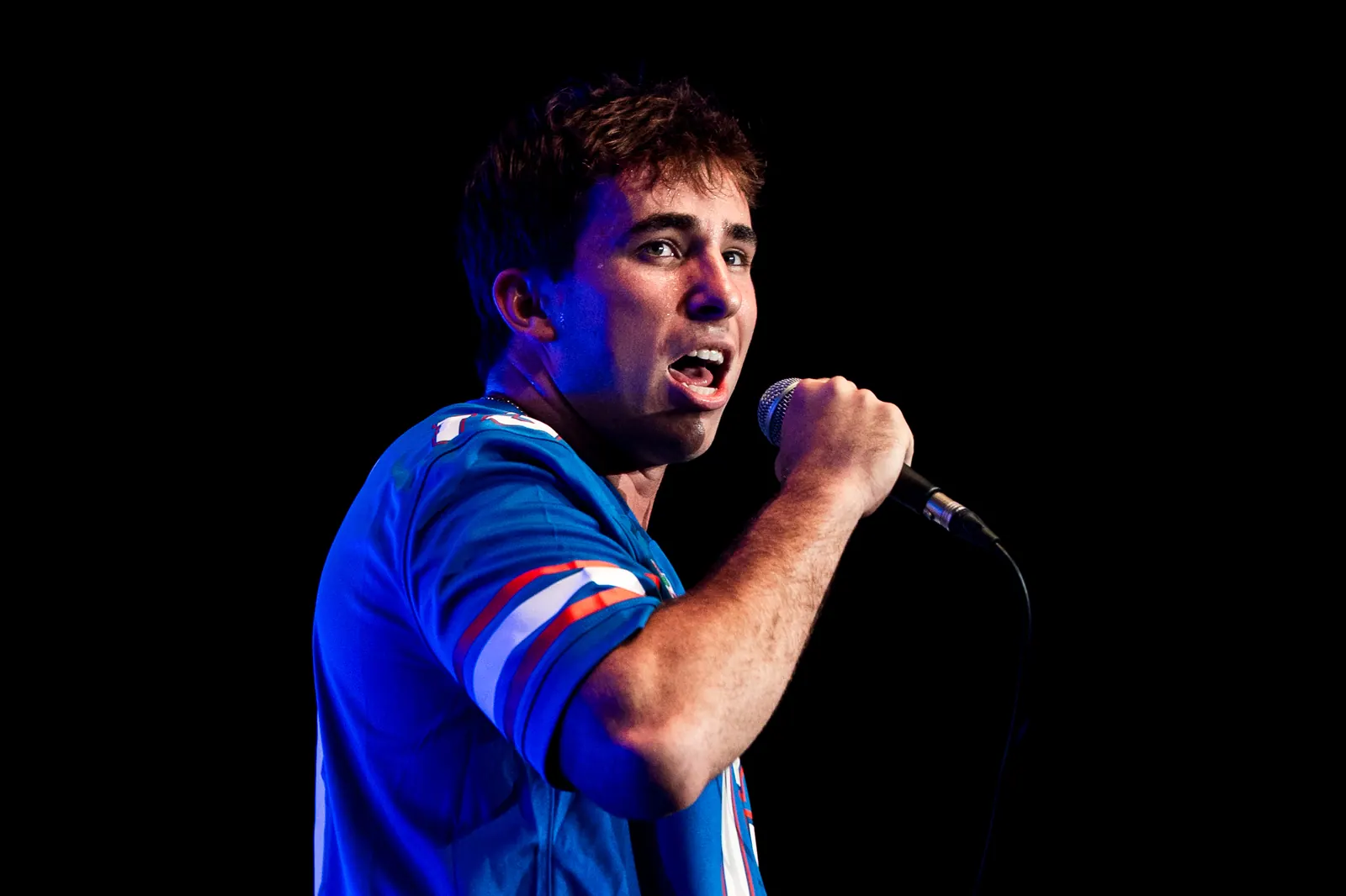 The vocalist mid-lyric under deep blue light, turned toward the crowd.