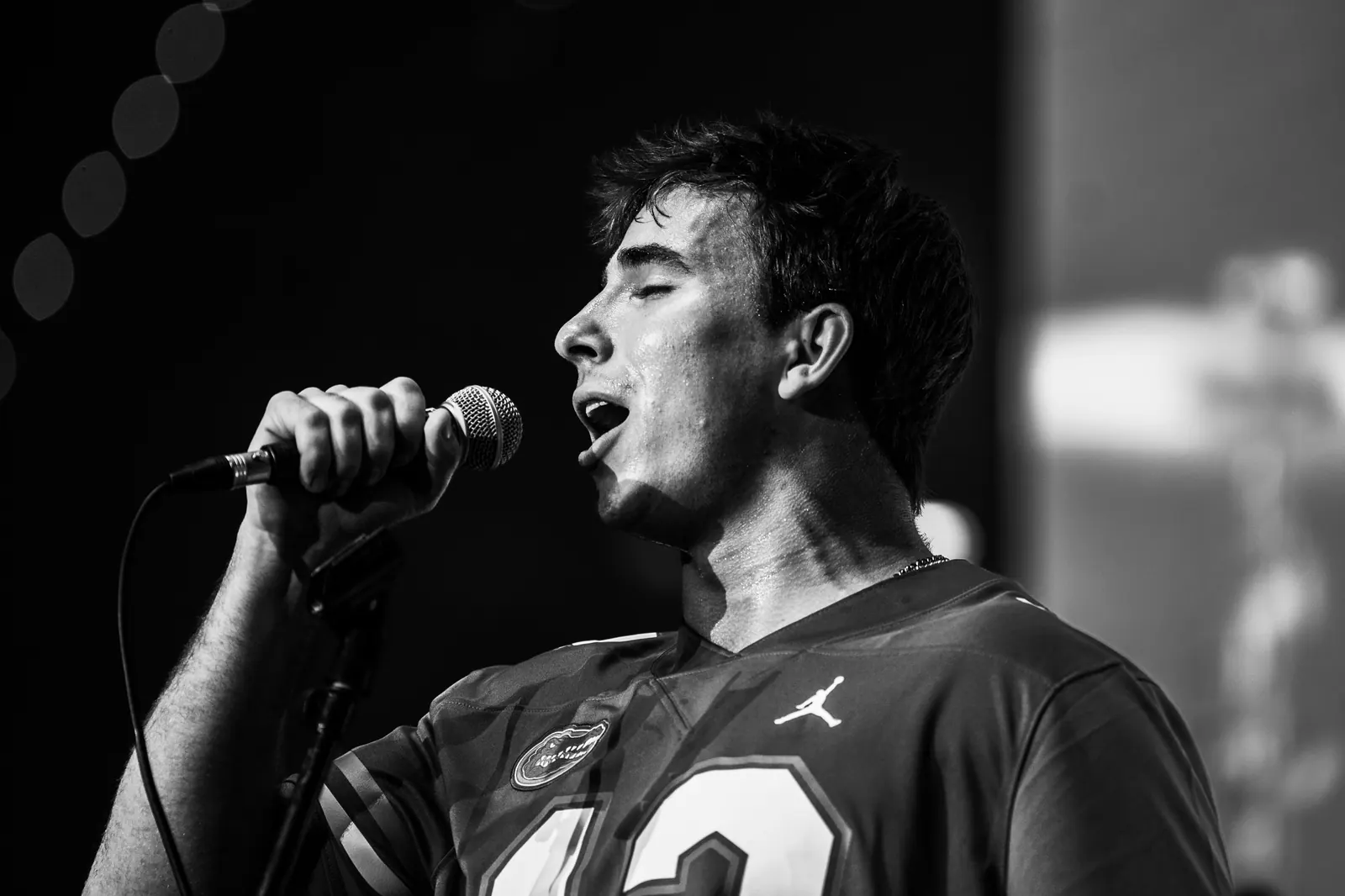 Black and white profile of the vocalist singing into the microphone in a Gators jersey.