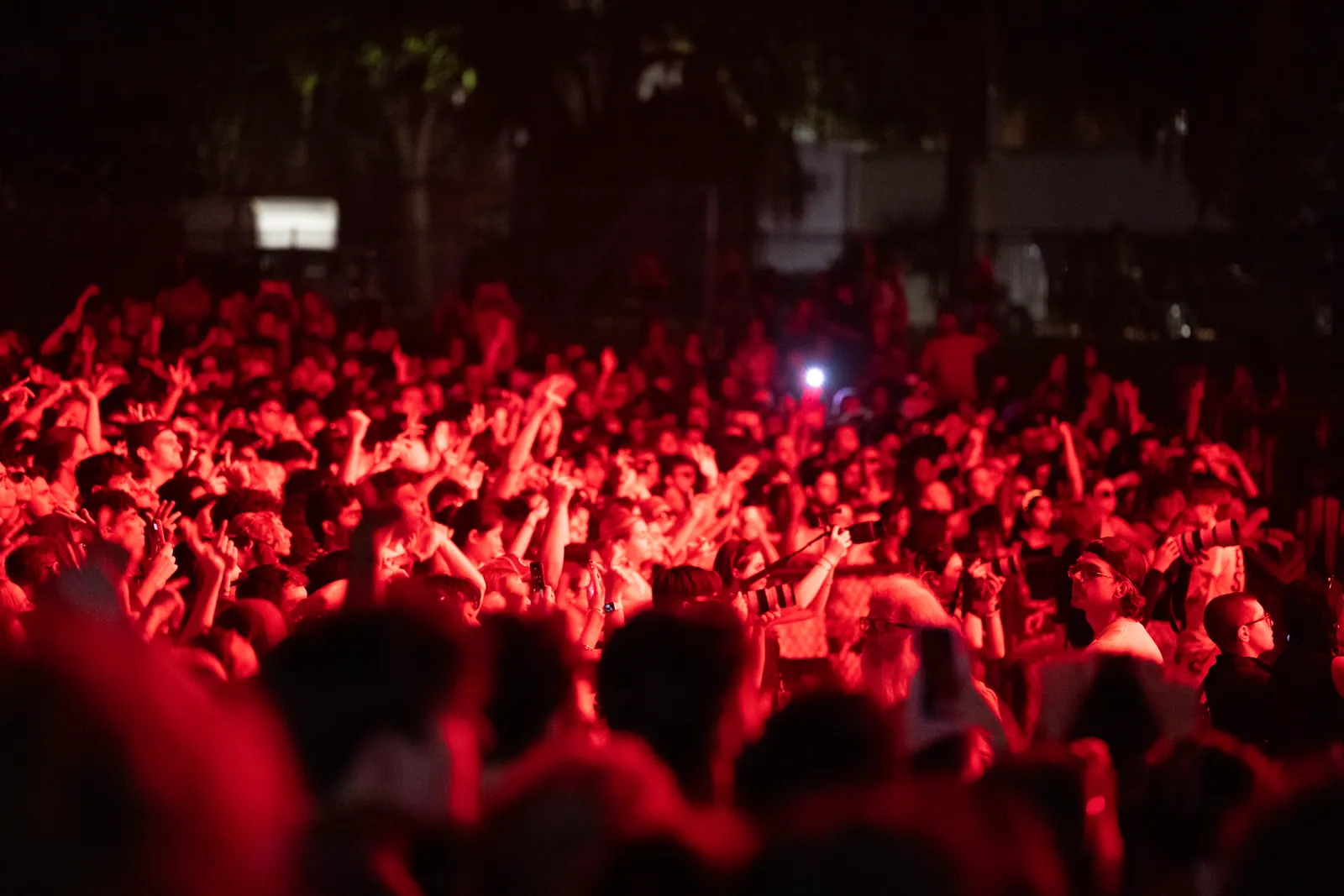 Close view into the crowd bathed in red light, arms up.