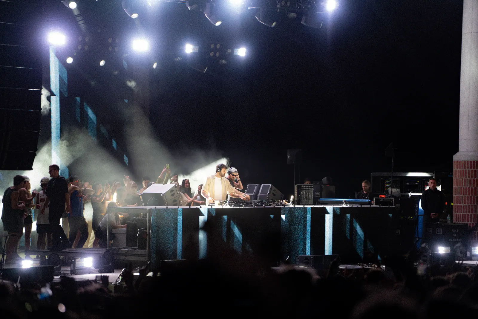 The main stage under white beams and haze, DJs at the decks and the crowd in the foreground.