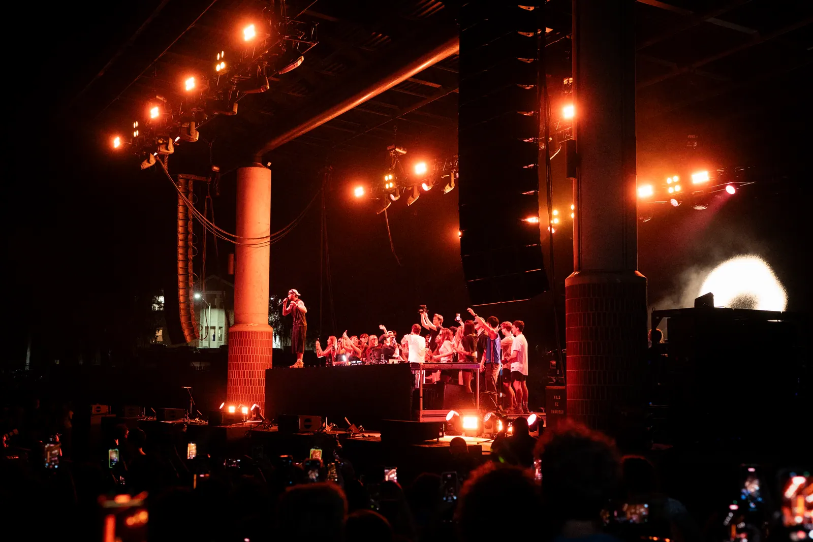 Wide view of the stage under strings of orange lights, the crowd silhouetted in front.