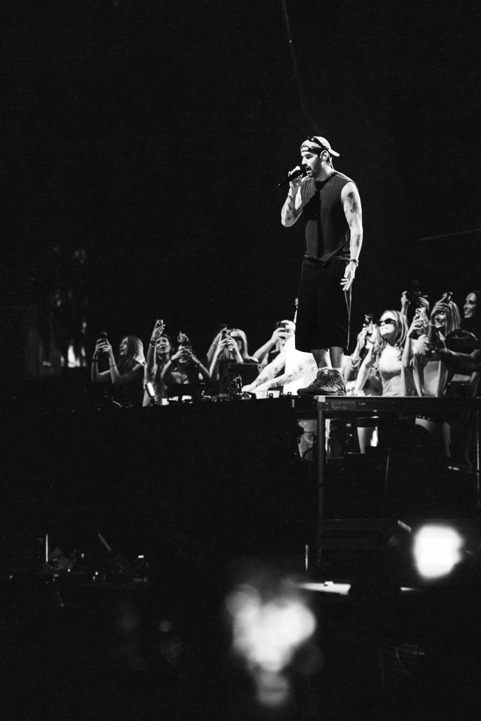 Black and white, a performer at the stage edge above a crowd holding up their phones.